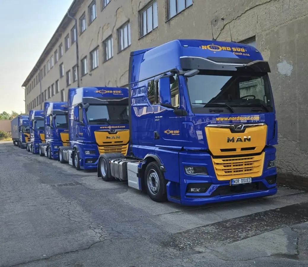Zwei Scania-Lkw mit blauer Lackierung und gelben Akzenten, die bei Dämmerung geparkt sind, mit eingeschaltetem Scheinwerferlicht.